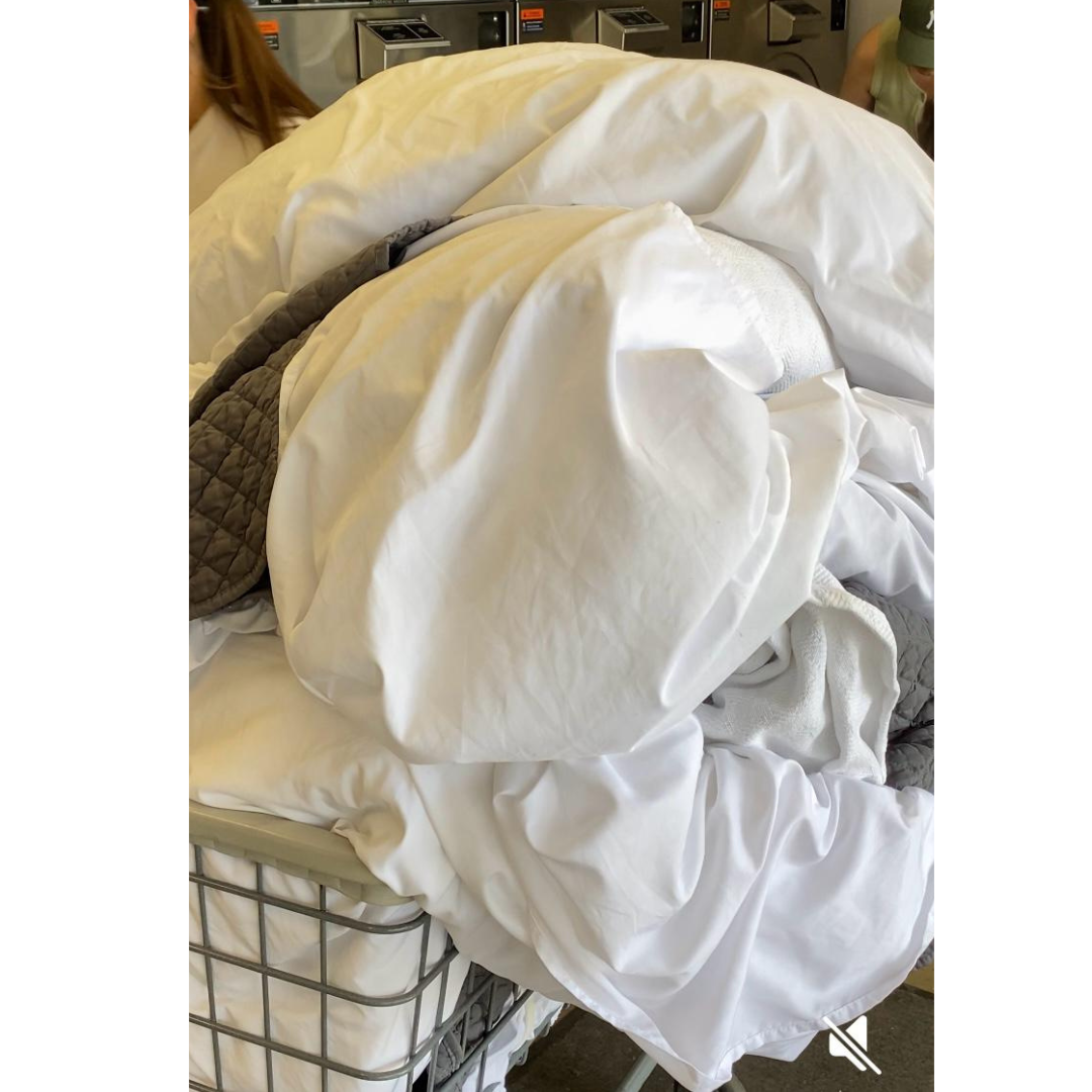 Folded white linens and towels in laundry basket, Sprinkle Laundry wash and fold service.